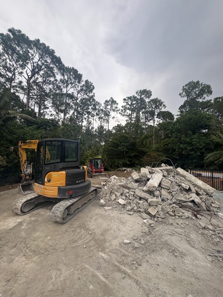 Excavator and track loader beside a pile of broken concrete and rebar during demolition and debris removal in Southwest Florida