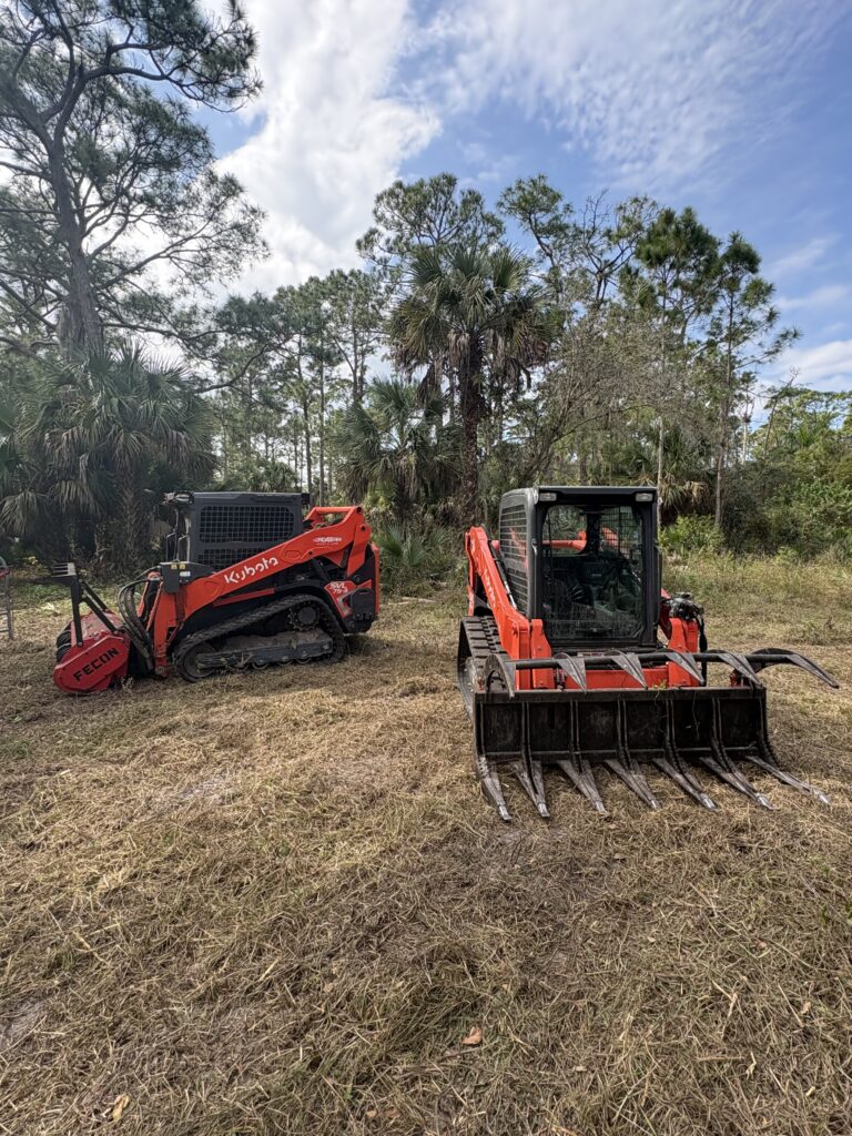 Two Kubota track loaders with a forestry mulcher and root grapple on a wooded lot in Southwest Florida