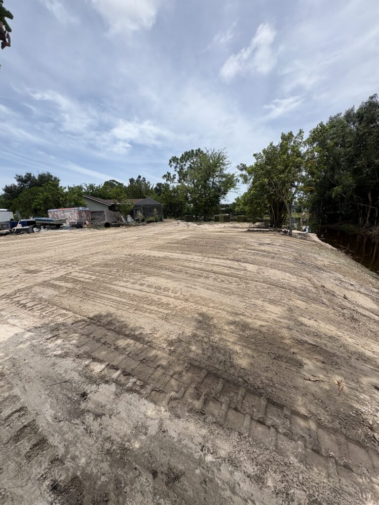 Large waterfront lot cleared and graded to a wide, level dirt pad along a canal in