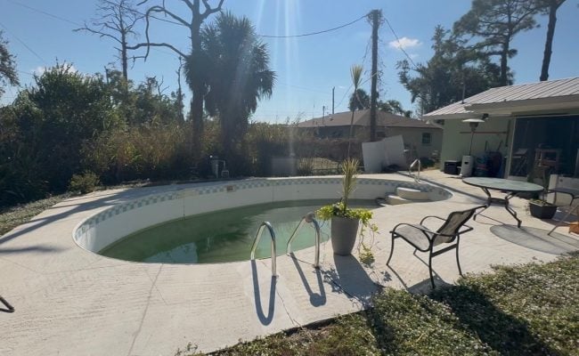 Old kidney-shaped pool with green water before pool demolition and removal in Southwest Florida