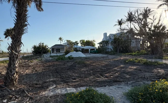 Cleared and graded coastal beachfront lot with a fill pile staged near waterfront homes in Southwest Florida